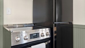 Een keuken met een roestvrijstalen fornuis, oven en een zwarte koelkast.