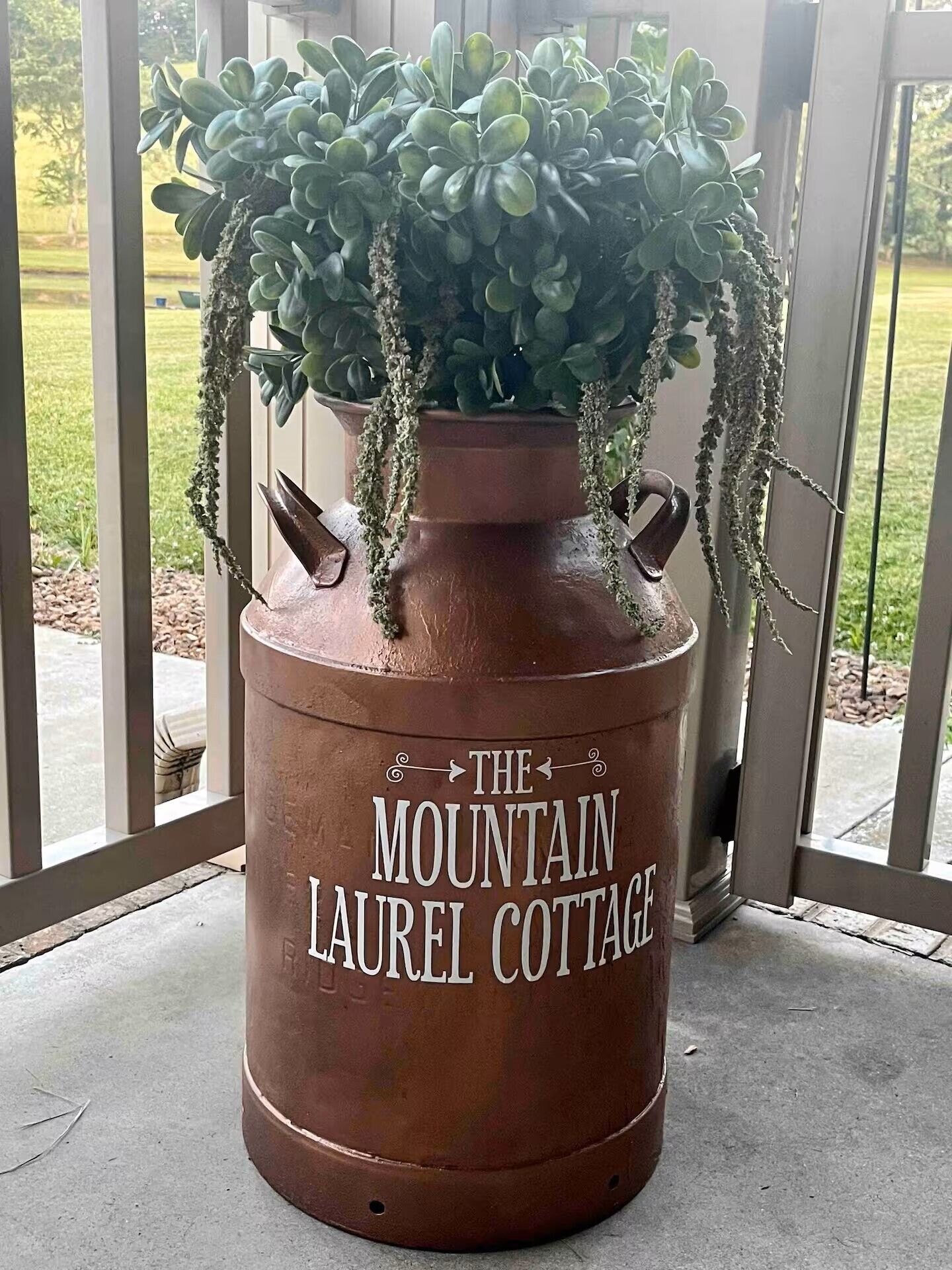 Una maceta de terracota grande con una planta suculenta y enredaderas colgantes, con la etiqueta 'The Mountain Laurel Cottage'.