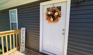 Uma casa com porta branca, um letreiro de boas-vindas e uma coroa de flores na porta.