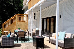 Eine überdachte Terrasse mit Korbmöbeln, einer Feuerstelle und einer Treppe, die zu einer oberen Ebene führt.