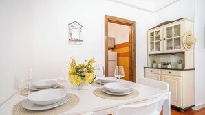 Zona de menjador amb taula blanca, quatre plats i un vas amb flors grogues.