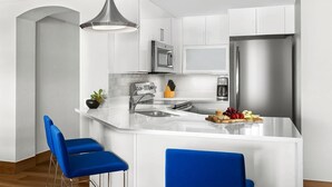 Una cocina moderna con armarios blancos, electrodomésticos de acero inoxidable, una isla central con taburetes y una pequeña planta en la encimera.