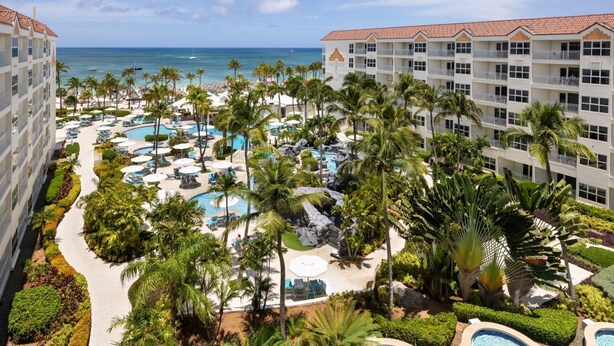 Un resort con varias piscinas, palmeras y vista al océano.