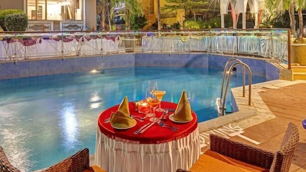 A poolside area with a table set for dining, surrounded by wicker chairs.