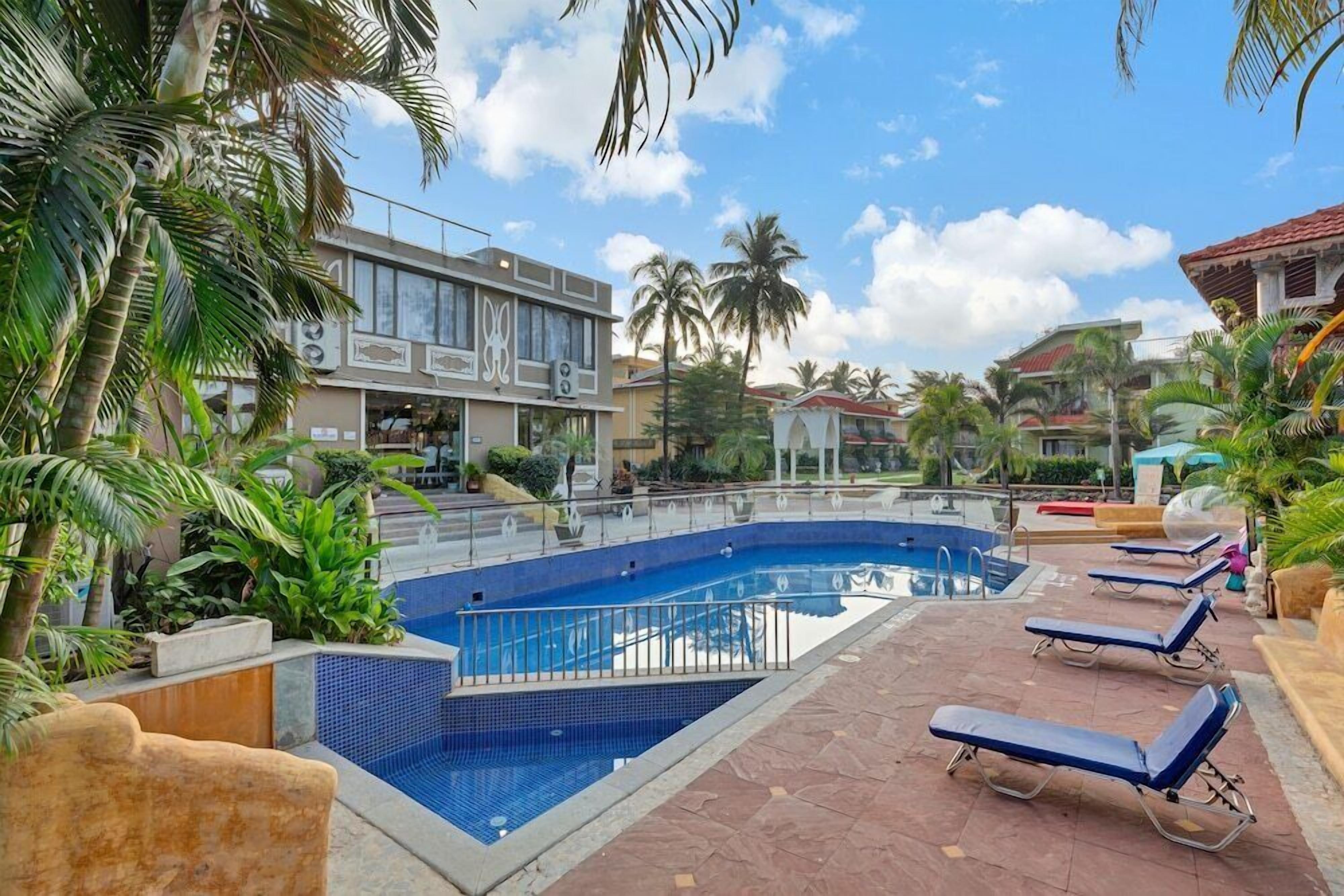 A swimming pool with lounge chairs, palm trees, and a building with large windows.
