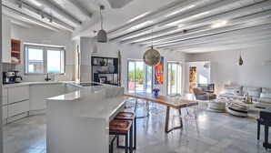 Una cocina moderna con una isla central, taburetes de bar y un comedor con sillas traslúcidas.