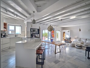 A modern kitchen with a central island, bar stools, and a dining area with clear chairs. - Stunning villa with pool, terrace and sunset view for 10 people in Ambelas (Naousa)