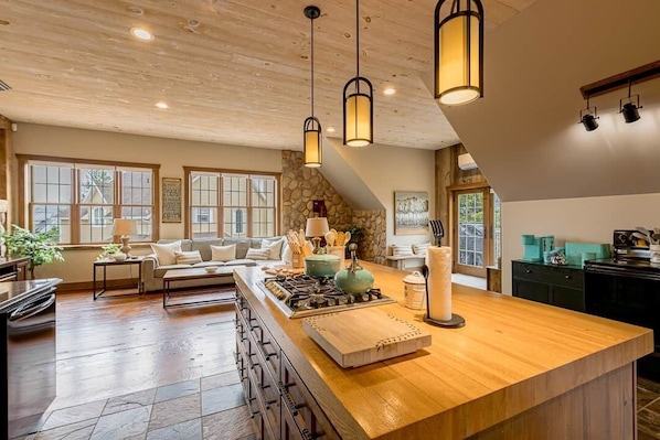 A spacious kitchen with a large island, wooden ceiling, and pendant lighting.
