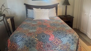 A bed with a patterned bedspread, a bedside lamp, and a window with blinds. - Beachfront Cottage Sleeps up to 4 Unit A (Indian Rocks Beach)