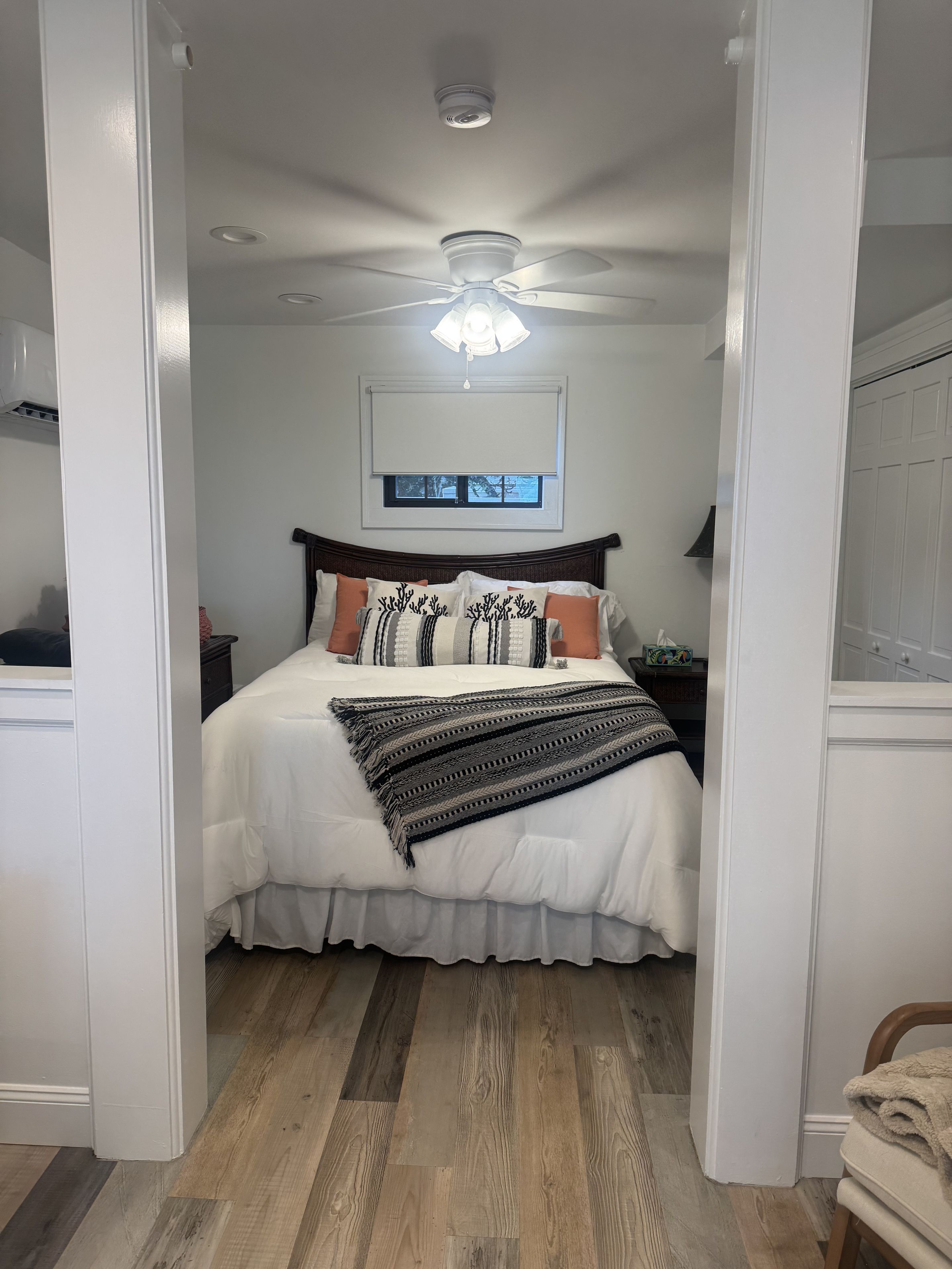 Un dormitorio con una cama, ventilador de techo, ventana y mesita de noche.