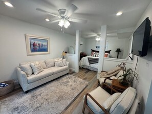 A modern living room with a sofa, a chair, a bed, and a television. - Beach Bougie Retreats - Unit A (Indian Rocks Beach)