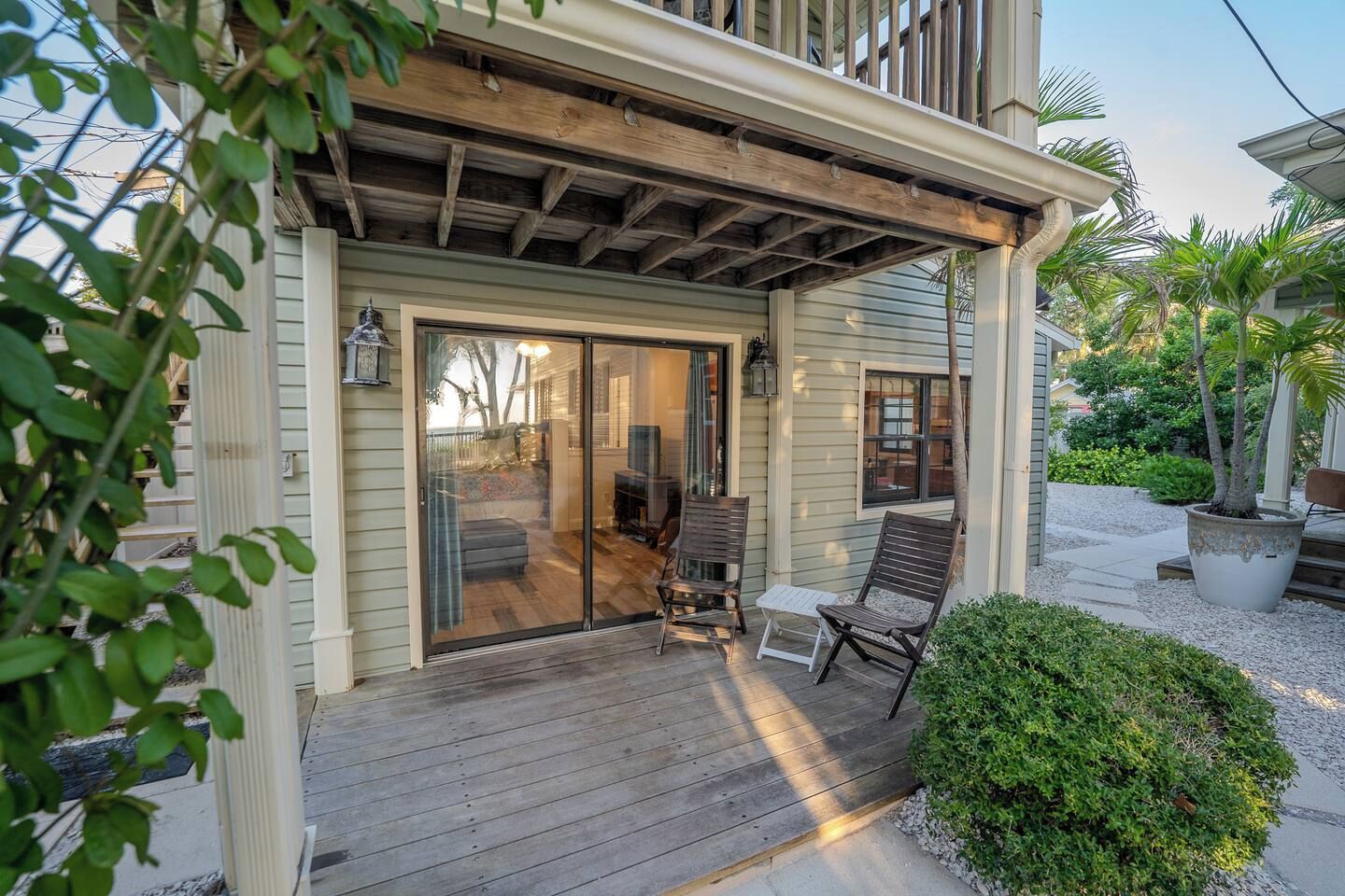Eine überdachte Veranda mit Holzterrasse, eine Schiebetür zu einem Innenbereich und Gartenmöbel.