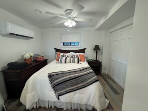 A bedroom with a bed, a ceiling fan, a wall-mounted air conditioner, a bedside table with a lamp, and a wardrobe. - Beach Bougie Retreats - Unit A (Indian Rocks Beach)