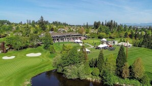 A golf course with a pond, a clubhouse, and surrounding trees.