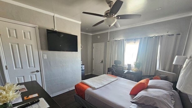 A hotel room with a bed, desk, chair, television, and a ceiling fan.