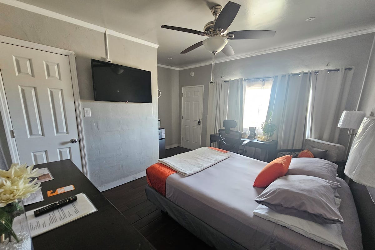 Ein Hotelzimmer mit Bett, Schreibtisch, Stuhl, Fernseher und Deckenventilator.
