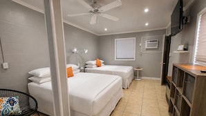 A hotel room with two beds, a ceiling fan, a TV, a small table, and a chair.