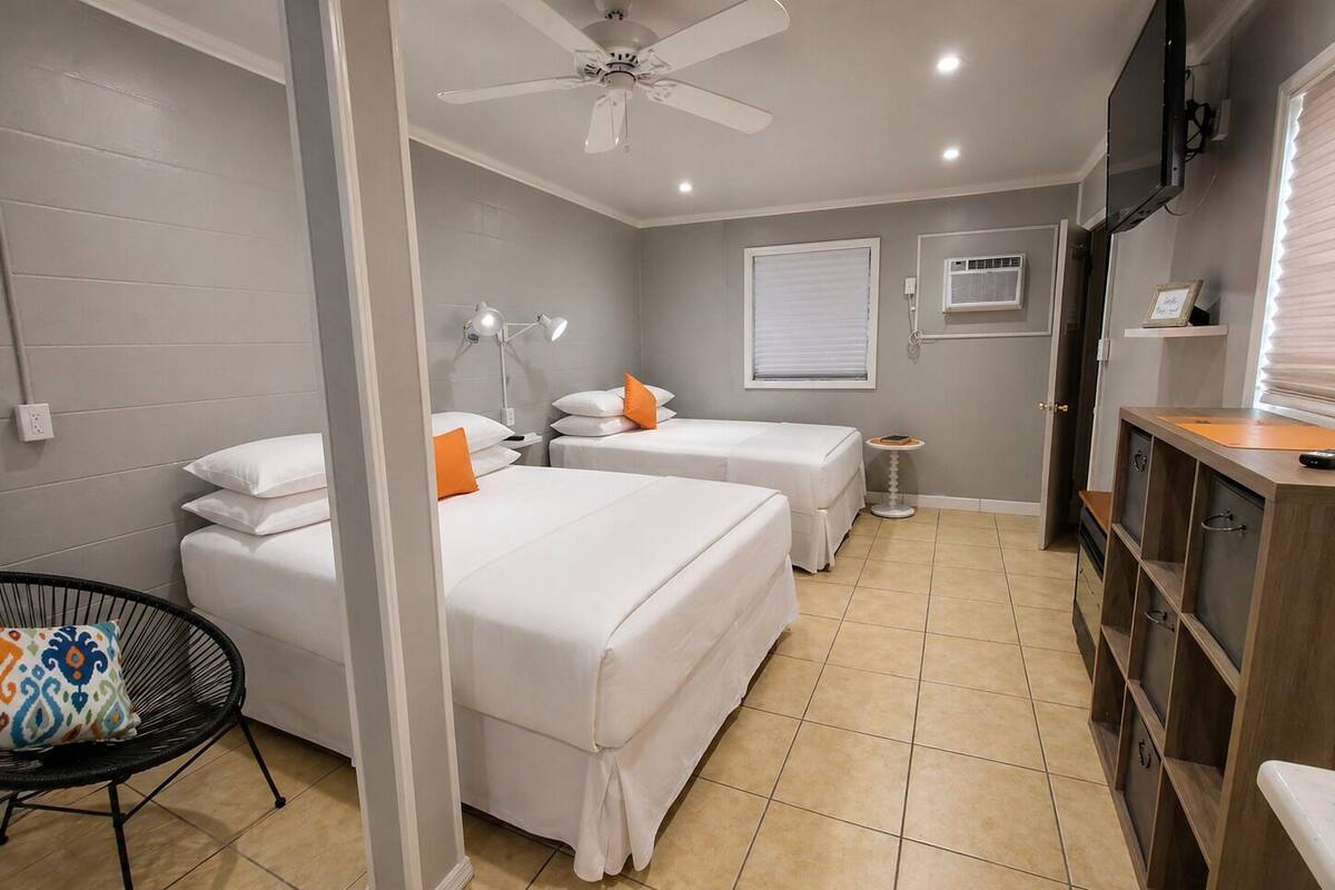 Ein Hotelzimmer mit zwei Betten, einem Deckenventilator, einem Fernseher, einem kleinen Tisch und einem Stuhl.