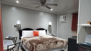 Un dormitorio con una cama, dos mesitas de noche, un ventilador de techo, un aire acondicionado montado en la pared y una pequeña mesa con sillas.