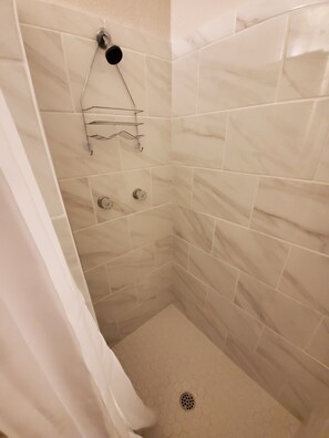 Eine Dusche mit weißen Fliesen, einem Duschvorhang und einem Metallregal mit Haken.
