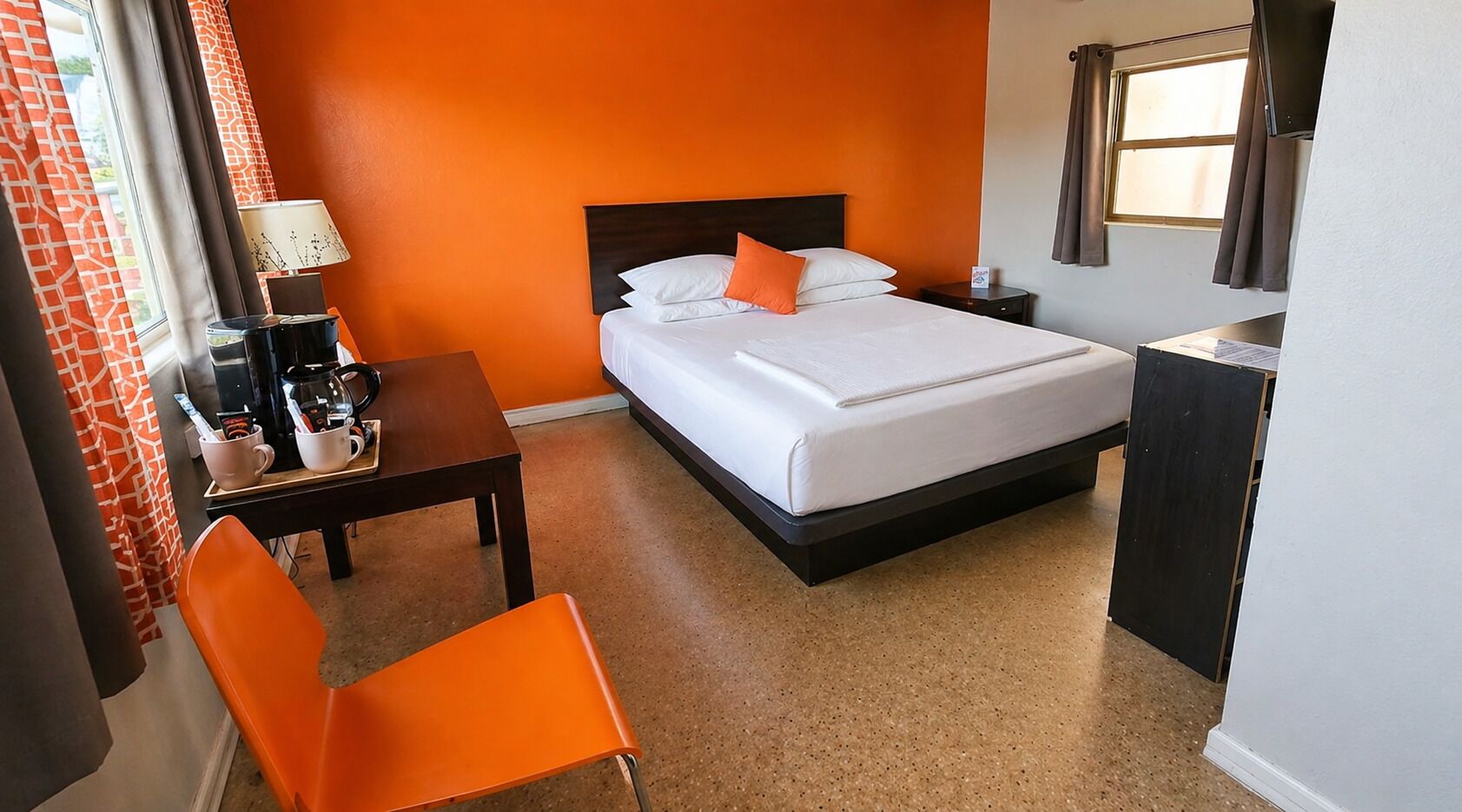 Habitación de hotel con cama, escritorio con lámpara, una silla y ventana con cortinas.