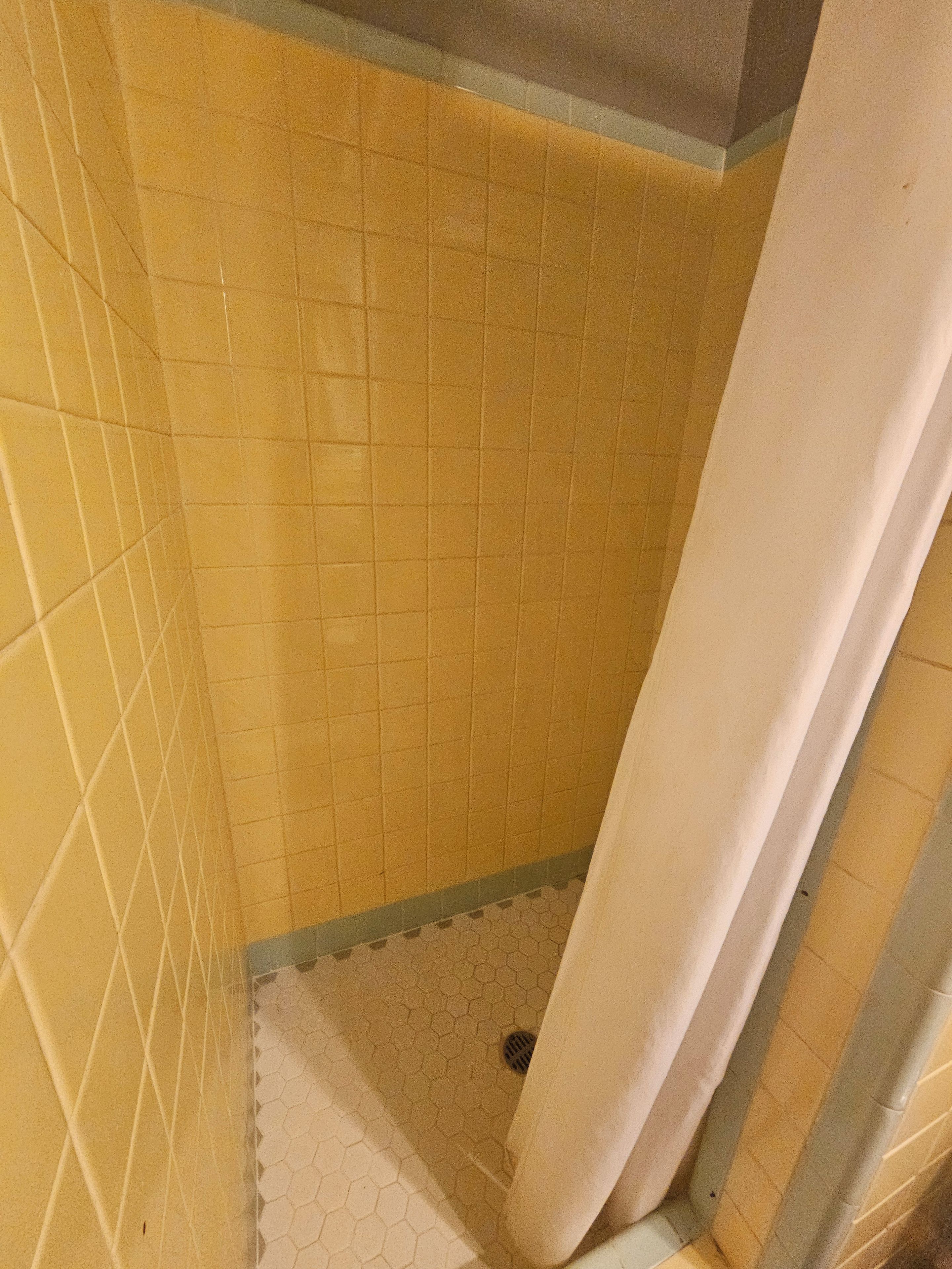 Een badkamer met gele betegelde wanden en een witte douchegordijn.