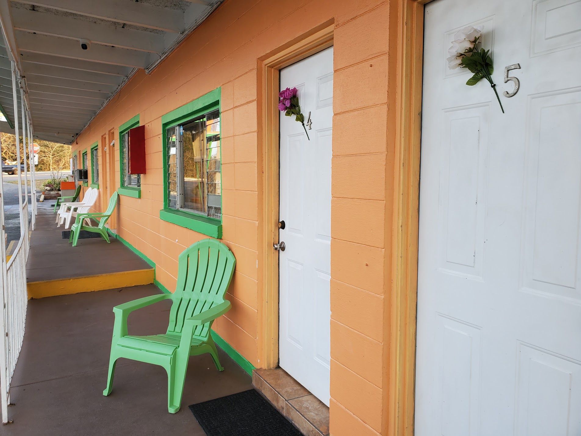 A motel with a porch, green chairs, and a white door with a number.