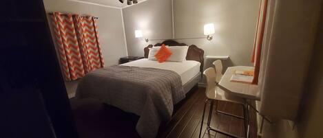 A hotel room with a bed, a desk, a chair, a ceiling fan, and a nightstand.