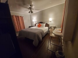 Een hotelkamer met een bed, bureau, stoel, plafondventilator en nachtkastje.