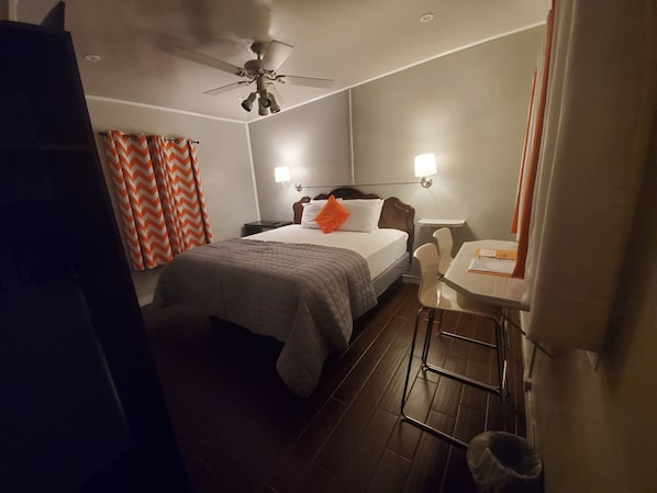 Una habitación de hotel con cama, escritorio, silla, ventilador de techo y mesita de noche.