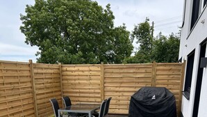 Eine Terrasse mit Tisch und Stühlen, ein überdachter Grill und ein Holzzaun.