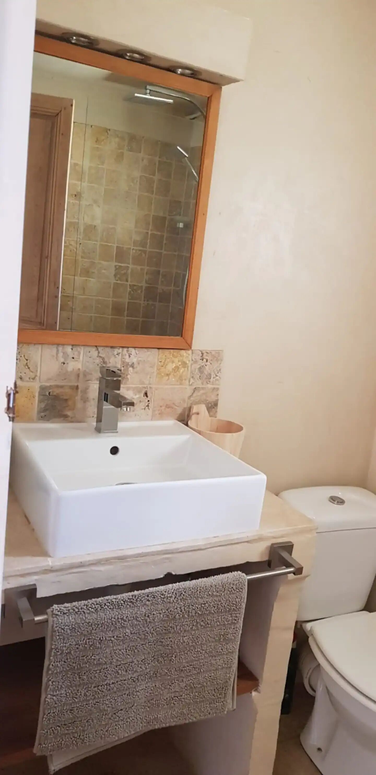 Un baño con lavamanos blanco, espejo, toallero y retrete.