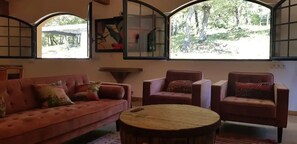 A living room with a sofa, two armchairs, a round coffee table, and large windows with a view of greenery. - Private Estate for 18 guests • Pool • Provence • No neighbours (Signes)