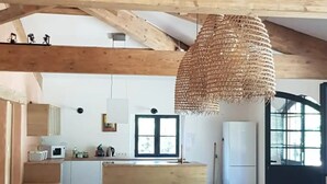 Eine geräumige Küche mit Holzbalken, einem Essbereich mit langem Tisch und Stühlen sowie einer hängenden Leuchte.