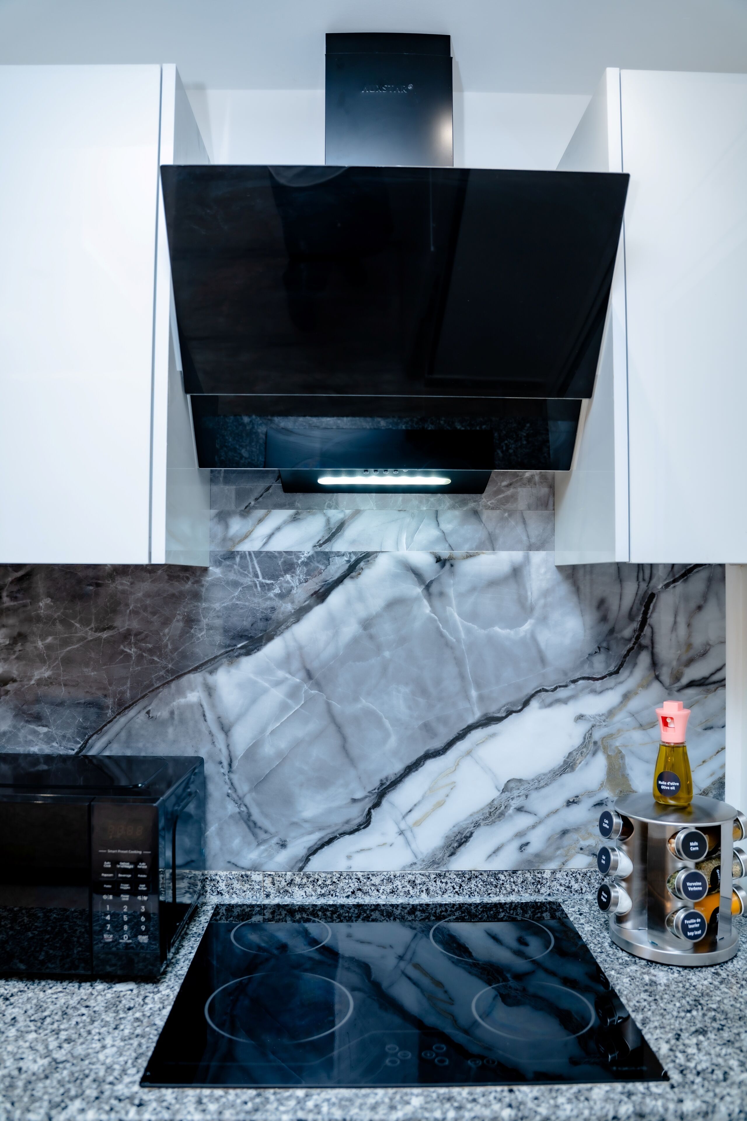 A kitchen with a black range hood, a microwave, an induction cooktop, and a marble backsplash.