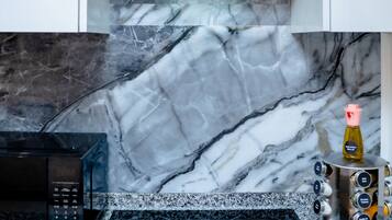 A kitchen with a black range hood, a microwave, an induction cooktop, and a marble backsplash.