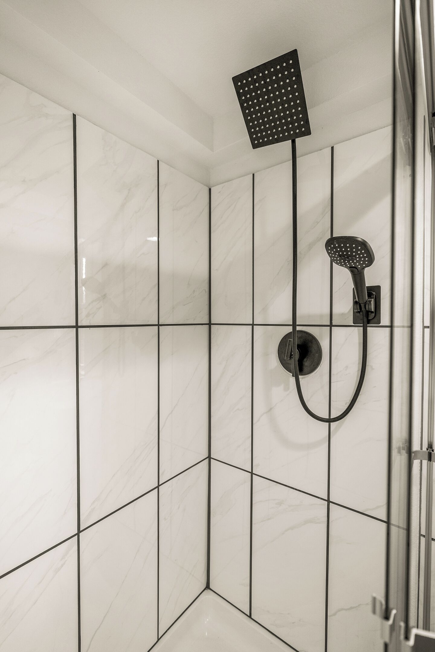 Un bagno moderno con piastrelle in marmo bianco, un soffione a mano e un rubinetto montato a parete.