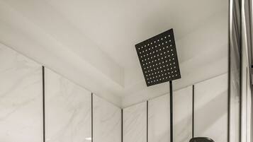 Un bagno moderno con piastrelle in marmo bianco, un soffione a mano e un rubinetto montato a parete.
