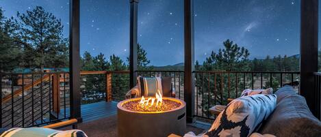 A covered outdoor area with a fire pit, seating, and a starry night sky view.
