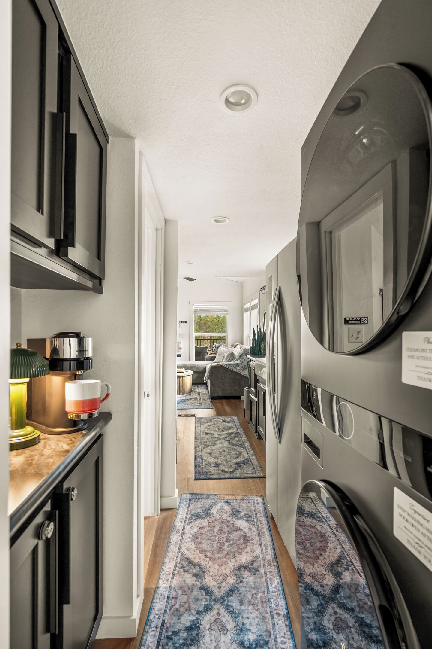A modern kitchen with stainless steel appliances, a coffee machine, and a view to a living area.