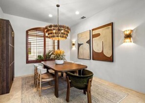 A dining area with a wooden table, chairs, a hanging light fixture, and abstract wall art. - Palm Desert luxury 3-bed+ home. Golf Cart, pickleball etc, in Rancho La Quinta (La Quinta)