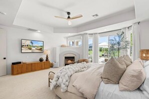 Ein Schlafzimmer mit Bett, Kamin, Deckenventilator und einem großen Fenster.