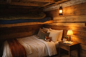 Une chambre confortable, aménagée dans le style d’un chalet, avec un lit superposé, une table de chevet avec une lampe et un jouet en peluche sur le lit.