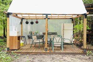Une structure en bois comprenant une table et des chaises, un réfrigérateur et des pots suspendus.