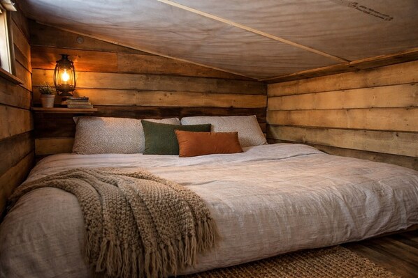 Une chambre dans une cabane en bois, avec un lit, des oreillers, une couverture et une lampe fixée au mur.