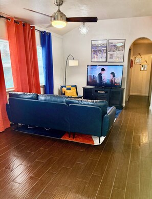 Ein Wohnzimmer mit blauem Sofa, Fernseher, Deckenventilator und einer Kristallleuchtre.