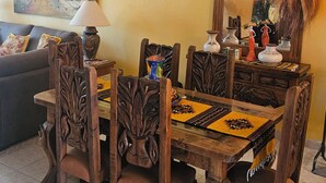 Un coin repas avec une table et des chaises en bois, un ventilateur de plafond, un tableau au mur et un canapé à l’arrière-plan.