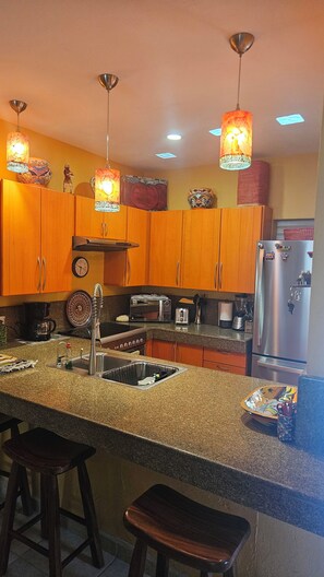 A kitchen with wooden cabinets, a stainless steel refrigerator, a sink, and bar stools. - Cozy 2-bedroom condo in perfect Bucerías with AC,  private rooftop bar area (Bucerías)