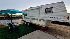 Un véhicule récréatif de la marque « Wildwood », doté d’un espace salon couvert et amarré au bord d’un plan d’eau.
