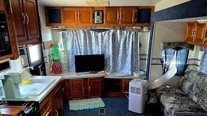 Une cuisine compacte pour camping-car, avec des placards en bois, une cuisinière, un évier et un téléviseur.